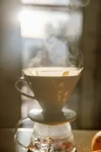Coffee filter with coffee grounds in a glass carafe on a wooden surface.