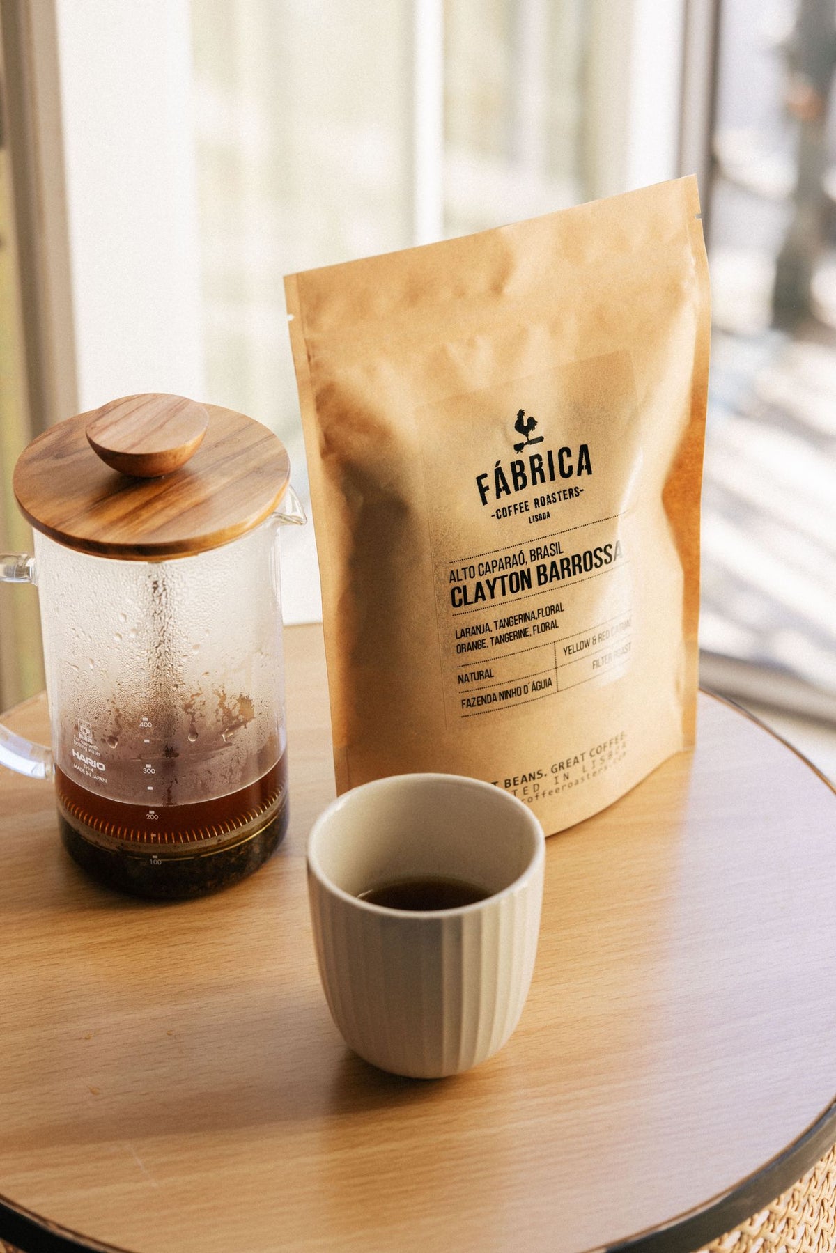 Fábrica coffee bag with a French press and cup on a wooden table.