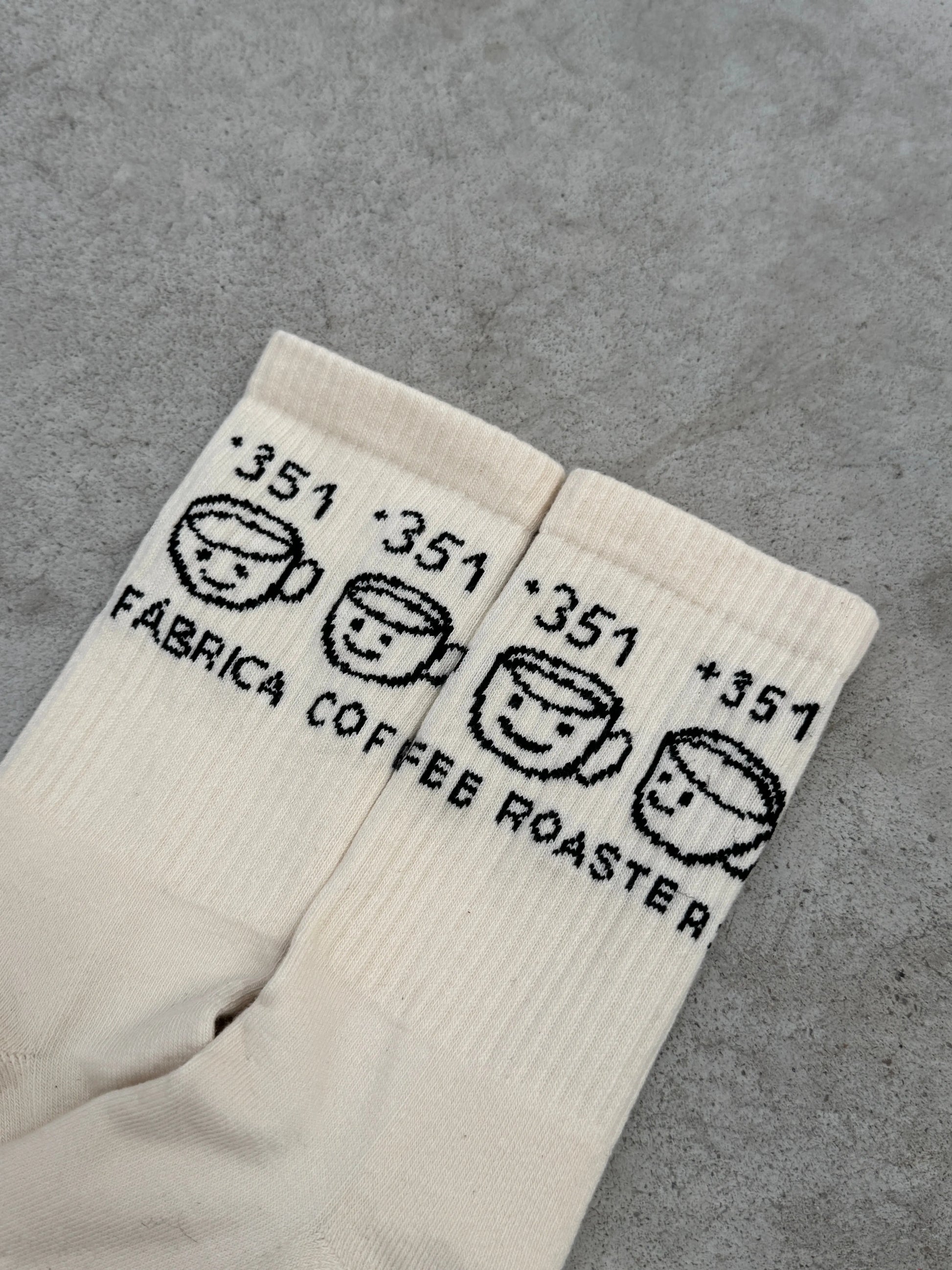 Pair of white socks with black text and smiley face designs on a gray surface